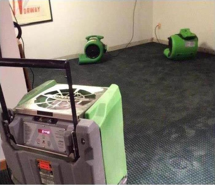picture of a carpeted basement with a couple Servpro fans and a dehumidifiers set up in there