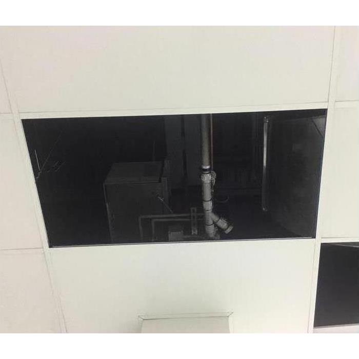picture of a missing ceiling tile with the ceiling pipes exposed