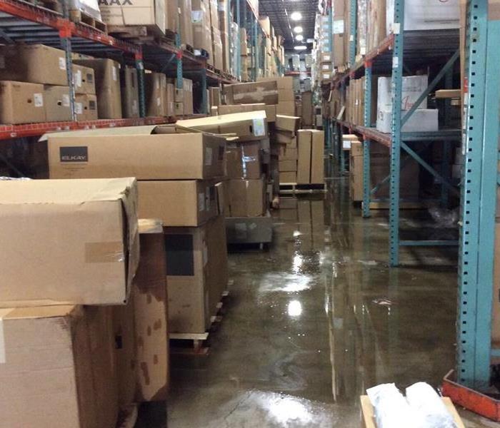 Warehouse with shelves full of boxes and water on the cement floor below 