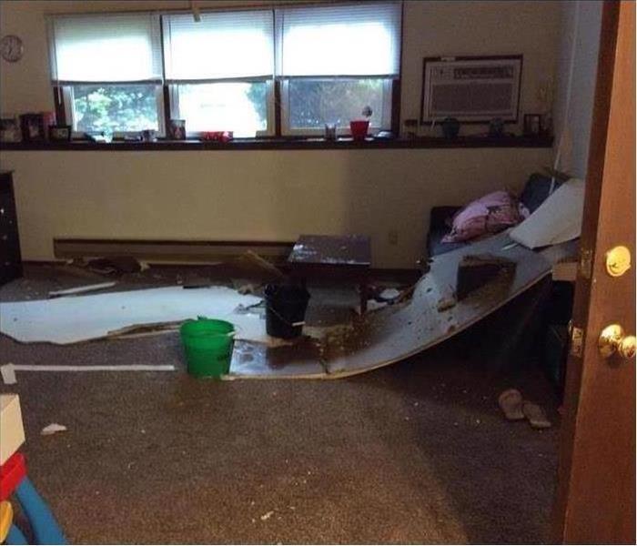 picture of an apartment with water damage, a bucket and ceiling debris scattered 